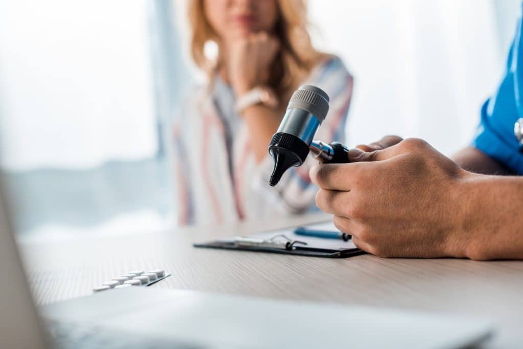 An audiologist holding an otoscope, preparing to examine a patient’s ear during a hearing evaluation.
